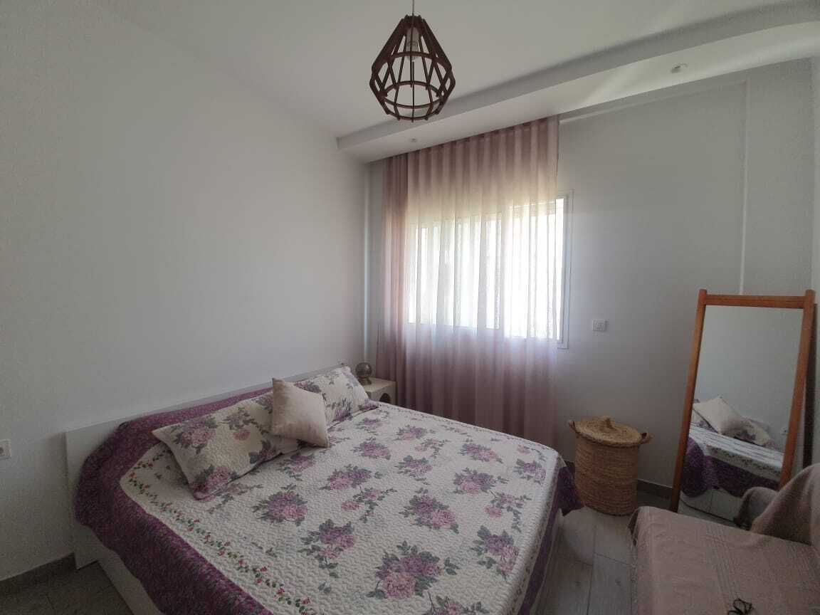 Ein Schlafzimmer mit einem Bett, einem Nachttisch, einem Spiegel und einem Fenster mit Vorhängen.