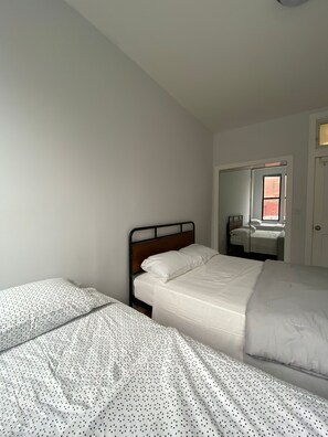 A bedroom with two beds, a wooden headboard, and a window with a view of a building outside.