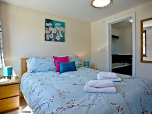 Une chambre à coucher avec un lit, des oreillers, une table de chevet, une lampe, une porte de salle de bain et un tableau au mur.