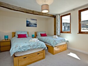 Un dormitorio con dos camas, una mesita de noche con lámpara, cabecero de madera, ventana con cortinas y un cuadro en la pared.