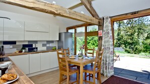 A modern kitchen with wooden beams, a dining area with a table and chairs, and a view of the outdoors.