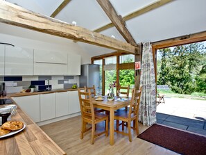 Une cuisine moderne avec des poutres en bois, un coin repas avec une table et des chaises, et une vue sur l’extérieur.