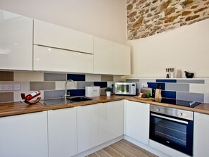 A modern kitchen with white cabinets, a wooden countertop, a built-in oven, a microwave, and a stone wall above. - 2 bedroom accommodation in Umberleigh (Umberleigh)