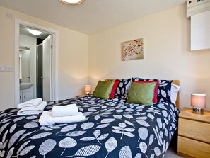 A neatly made bed with a leaf-patterned bedspread, a bedside lamp, and a wall-mounted artwork.