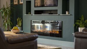 A modern living room with a fireplace, a flat-screen TV mounted on the wall, and a comfortable seating area with leather sofas.