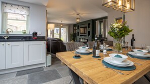 A modern kitchen with white cabinets, a wooden dining table set for four, and a chandelier above.