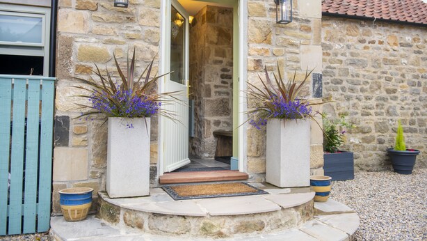 A stone building with a door leading to a room. There are two large planters with plants on either side of the door.