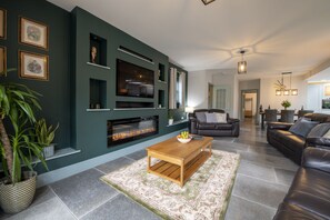 Un salon moderne doté d’une cheminée, de canapés en cuir, d’une table basse et d’un téléviseur à écran plat fixé au mur.