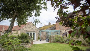 A stone house with a green roof, a garden with a lawn, and a pergola.