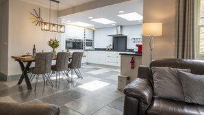 A modern kitchen with white cabinets, a dining area with a wooden table and chairs, and a leather sofa in the living room.
