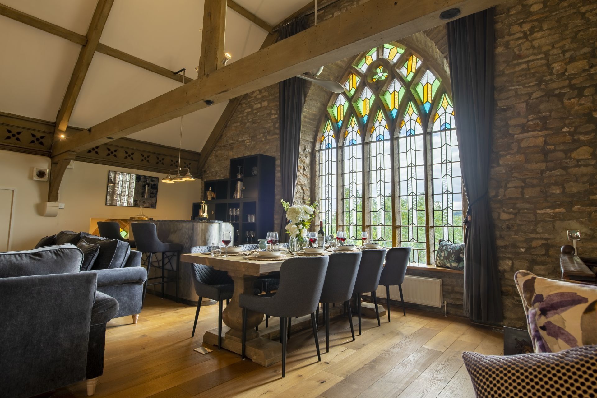 Uma sala de jantar com teto de madeira alto, paredes de pedra e uma grande janela de vitrais.