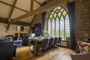 Uma sala de jantar com teto de madeira alto, paredes de pedra e uma grande janela de vitrais.