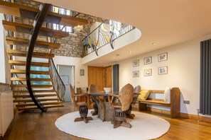 Uma sala de estar ampla com escada de madeira, uma mesa redonda e um banco.