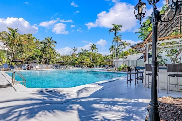 A swimming pool with lounge chairs, palm trees, and a pergola.
