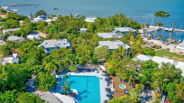 An aerial view of a resort with a central swimming pool, surrounded by lush greenery and multiple buildings. - 2BR Condo with Pool & Marina in Marathon (Marathon)