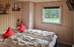 Ein Schlafzimmer mit einem Bett, einem Fenster, Holzwänden und einem Regal mit Dekoration.