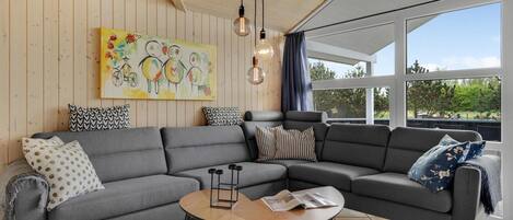 A modern living room with a grey sectional sofa, a round wooden coffee table, and a colorful children's painting on the wall.