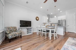 A modern kitchen with white cabinets, a stainless steel refrigerator, and a dining area with a wooden table and chairs.