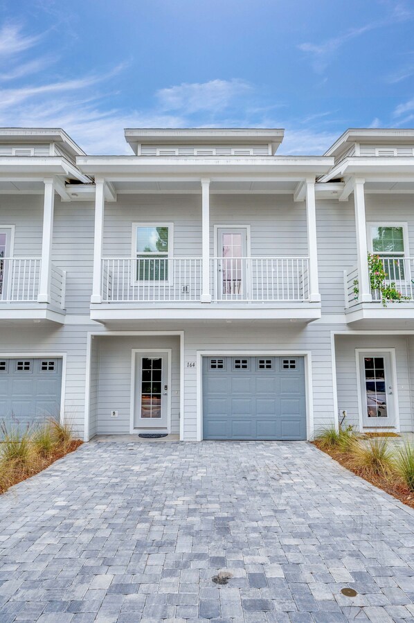 A two-story residential building with a paved driveway, a garage, and a balcony with a railing.