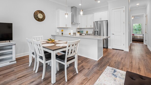 A modern kitchen with white cabinetry, a stainless steel refrigerator, and a dining area with a wooden table and white chairs. - Looking for privacy minutes from 30A? Look no further! Come stay with us! (Santa Rosa Beach)