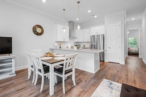 A modern kitchen with white cabinetry, a stainless steel refrigerator, and a dining area with a wooden table and white chairs.