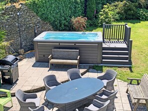 A hot tub with a wooden deck, wicker chairs, and a table.