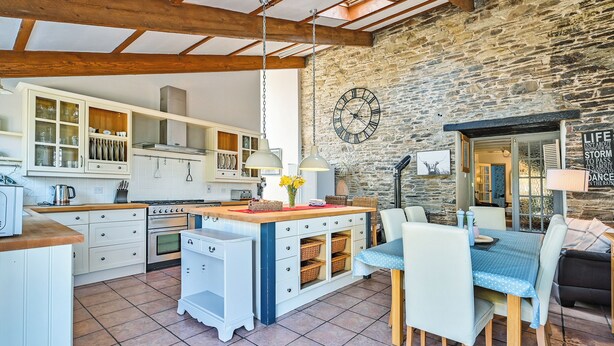 A kitchen with wooden beams, stone walls, and a dining area with a table and chairs. - The Old Farmhouse-UK12895 (Pelynt, near Looe)