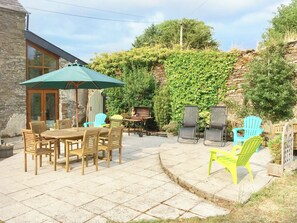 Eine Terrasse mit einem runden Holztisch und Stühlen, einem grünen Sonnenschirm und einem Grill.