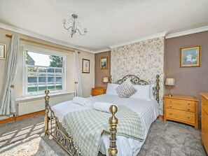 A bedroom with a four-poster bed, a chandelier, a window with curtains, a dresser, and a nightstand.