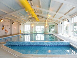 An indoor swimming pool with clear water, tiled walls, and overhead lighting.