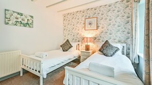 A bedroom with two beds, a nightstand, a lamp, a radiator, and a floral wallpaper. - The Old Farmhouse-UK12895 (Pelynt, near Looe)