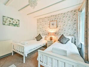 A bedroom with two beds, a nightstand, a lamp, a radiator, and a floral wallpaper.
