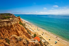 A coastal beach with clear blue waters, sandy shore, and rocky cliffs.