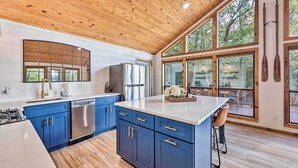 A modern kitchen with blue cabinets, a stainless steel refrigerator, and a large island. - 'Foxtail' Cabin Retreat: Steps to Beaver Lake! (Rogers)