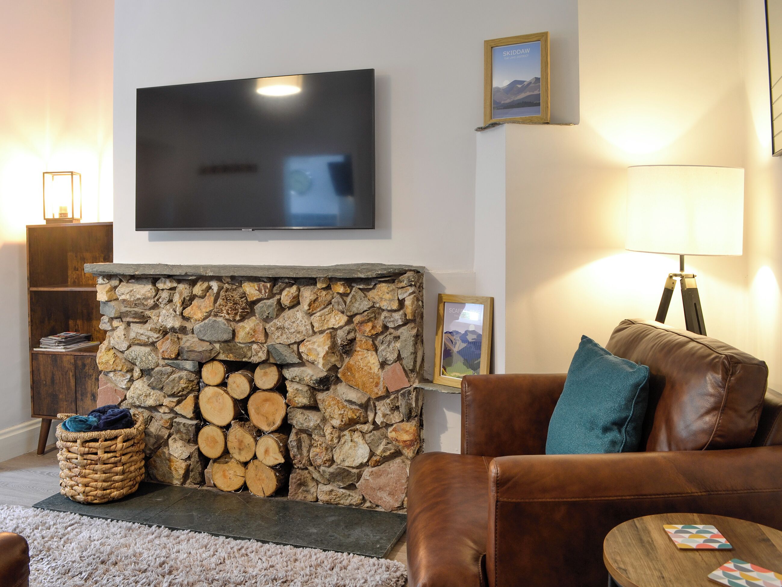 A living room with a stone fireplace, a television mounted on the wall, a brown leather sofa, and a small wooden table.