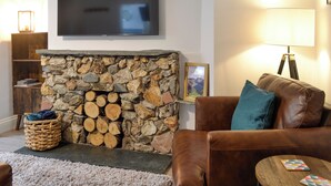 A living room with a stone fireplace, a television mounted on the wall, a brown leather sofa, and a small wooden table. - 2 bedroom accommodation in Hesket Newmarket, near Wigton (Hesket Newmarket, near Wigton)
