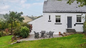 A white house with a grey roof, a front door, and a small porch with a table and chairs. - 2 bedroom accommodation in Hesket Newmarket, near Wigton (Hesket Newmarket, near Wigton)