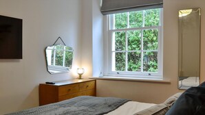 A bedroom with a bed, a dresser, a window with a view of greenery, and a mirror on the wall. - 2 bedroom accommodation in Hesket Newmarket, near Wigton (Hesket Newmarket, near Wigton)