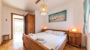A wooden bed with a headboard, two bedside tables, a hanging light fixture, and a painting of sailboats on the wall. - Luxurious home in Okrug Gornji (Okrug Gornji)