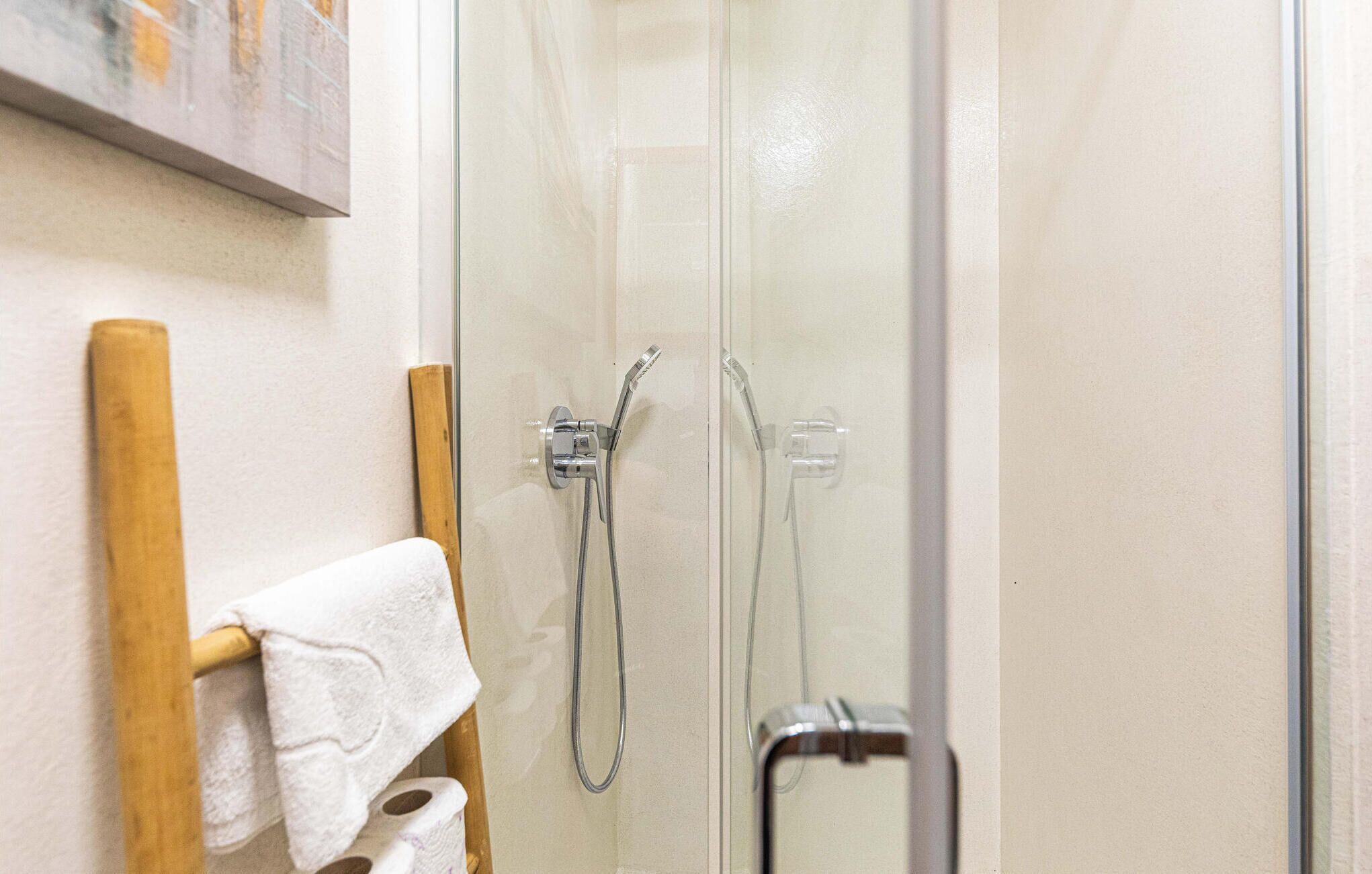Un espace douche clos par des parois de verre, avec un porte-serviettes en bois et une serviette blanche.