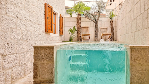 A pool with a stone wall on one side and wooden shutters on the windows. - Luxurious home in Okrug Gornji (Okrug Gornji)