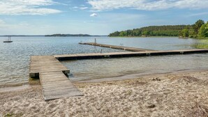 A wooden pier extending into a calm lake, with a sandy beach in the foreground and a forested island in the background.
