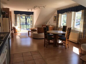 A cozy attic room with a dining table, chairs, a sofa, and a kitchen area.