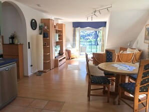 A spacious kitchen with wooden cabinets, a dining area with a round table and chairs, and a view of a balcony with curtains.