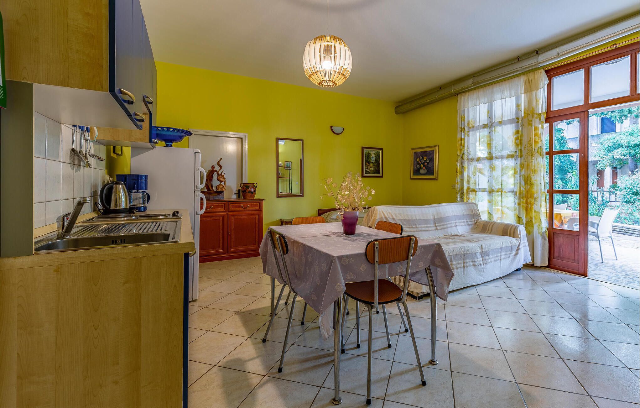 A bright kitchen with a dining area, a sofa, and a view of greenery outside.