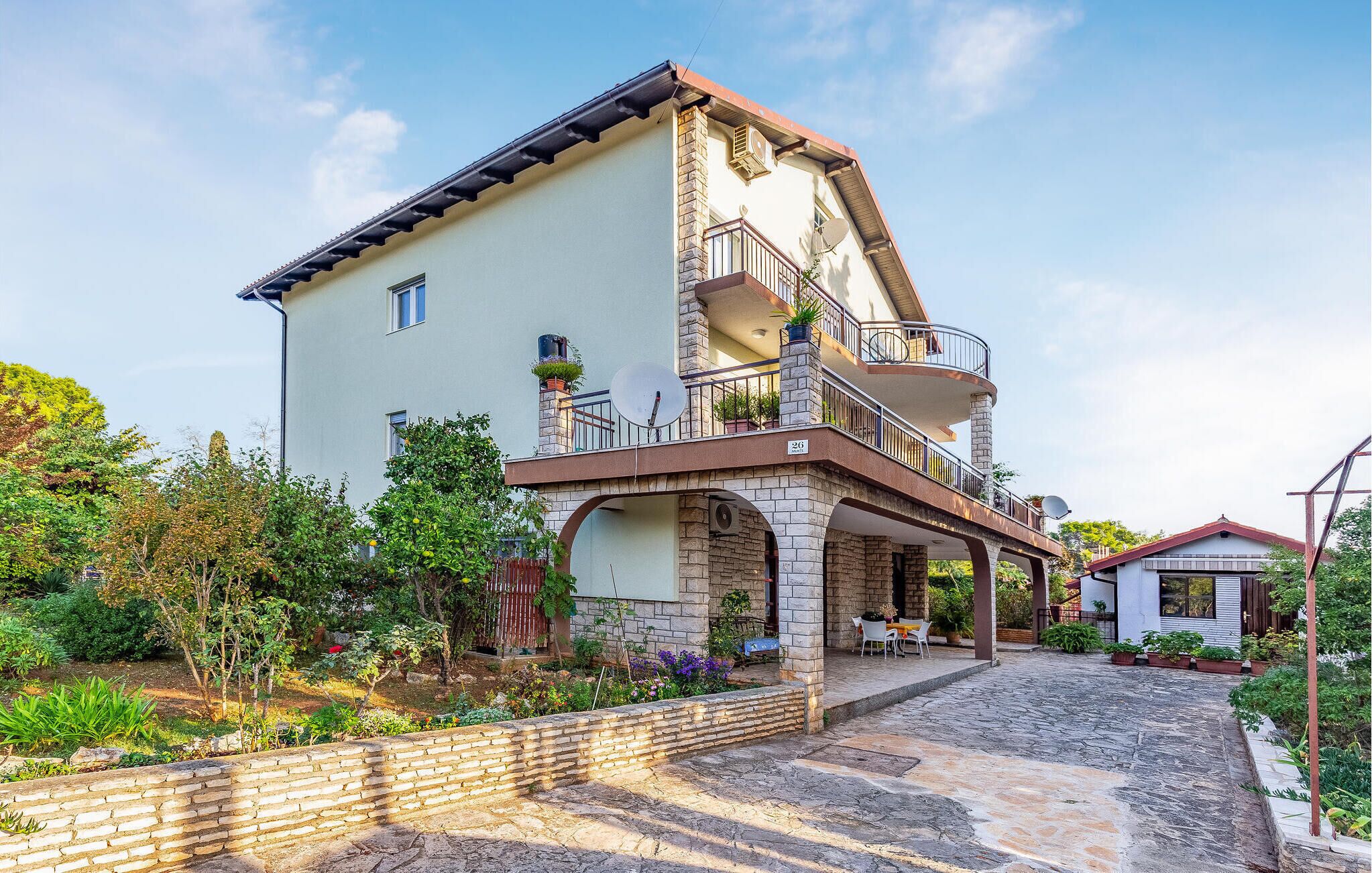 Une maison à deux étages dotée d’un balcon, d’une arche en pierre et d’un jardin.