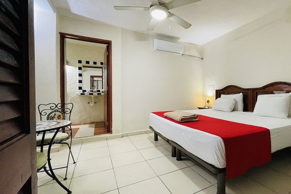 A hotel room with a bed, a desk, a chair, a ceiling fan, and an air conditioning unit.