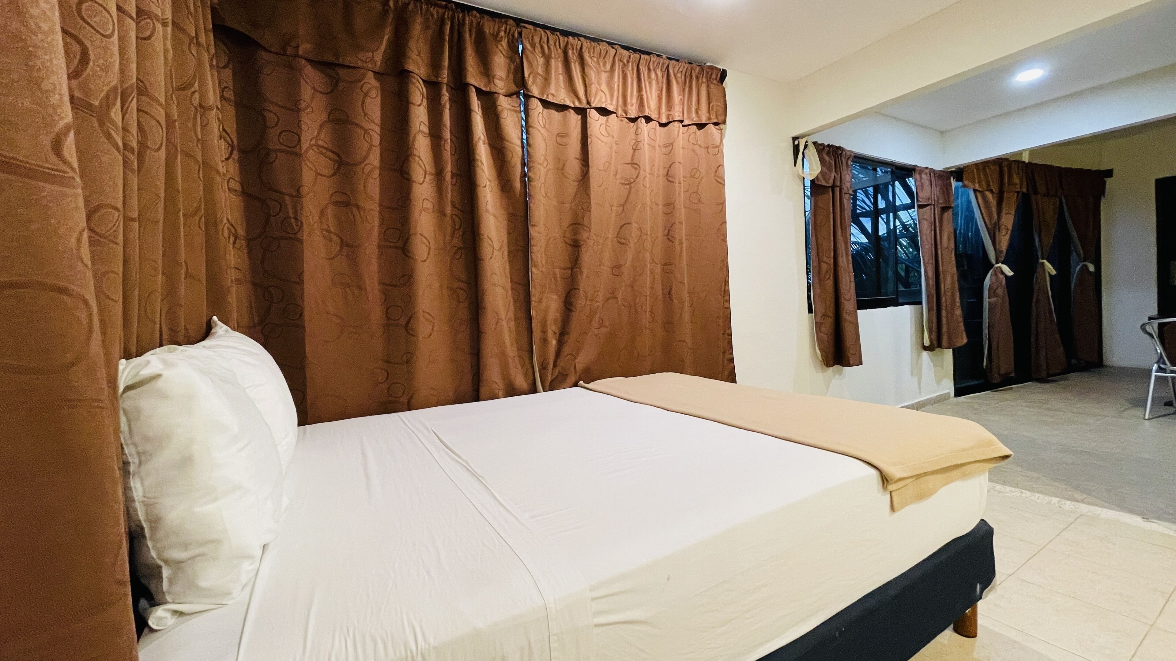 Une chambre à coucher avec un lit, des rideaux marron et une vue sur l’extérieur.