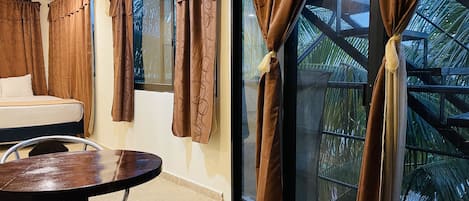 A room with a bed, a round table, and large windows with brown curtains.