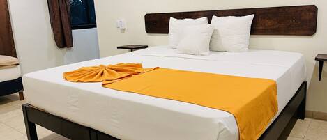 Una cama bien hecha con ropa blanca y un plaid amarillo, un cabecero de madera y una mesita de noche con una lámpara.